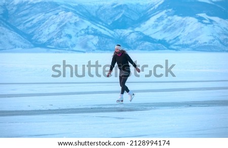 A young happy woman is skating on the transparent ice of the frozen Lake Baikal on a sunny winter day - World-famous figure skater "Polina Korobeynikova" performs on Lake Baikal