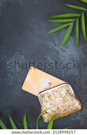 Gold wallet with gold credit card  on a black textured background with palm leaves and copy space. Concept of business, shopping, payment, finance and rich life