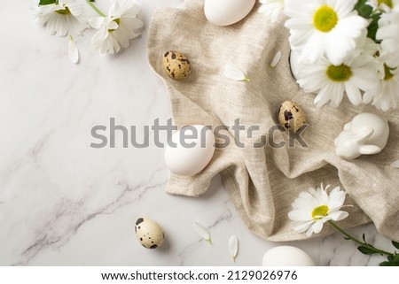 Top view photo of easter decorations bouquet of white chrysanthemum flowers petals ceramic easter bunny eggs and linen on isolated white marble texture background
