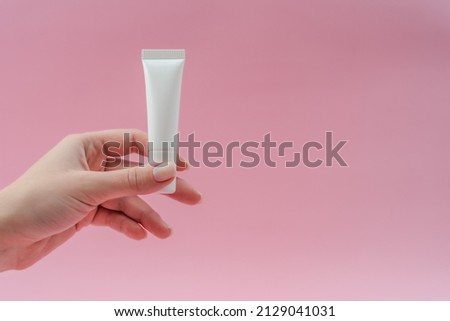 Woman's hand holds white plastic tubes on pink background. Сosmetic bottles for beauty or medicine products Royalty-Free Stock Photo #2129041031