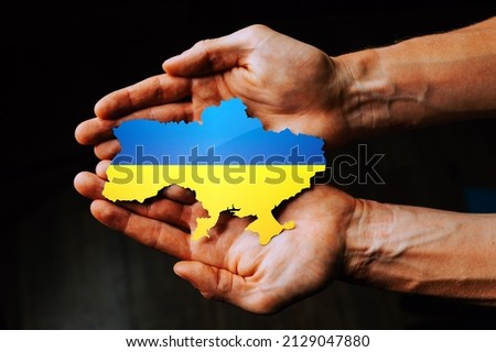 Support for Ukraine in the war with Russia. Hands holding the flag of Ukraine in the shape of the borders of Ukraine. Royalty-Free Stock Photo #2129047880