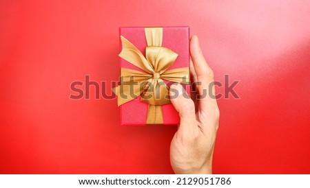 A man's hand holding beautiful Red gift box with gold ribbon on red background. Christmas and new year concept, Valentine Concept. Space for text.