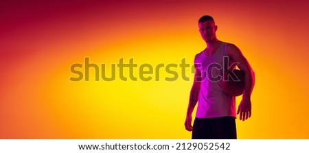 Studio shot of muscled sportive man, basketball player, danker isolated on gradient yellow purple background in neon light. Concept of sport, achievements, competition, hobby, active lifestyle.
