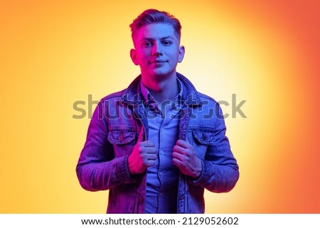 Style and beauty. Young handsome man wearing casual youth style clothes isolated on orange background in neon light, filter. Concept of emotions, facial expression, youth, aspiration, sales.