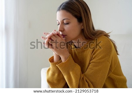 Spirituality and young people. Girl praying at home alone. Worried woman praying for strenght during russian invasion of Ukraine. Royalty-Free Stock Photo #2129053718