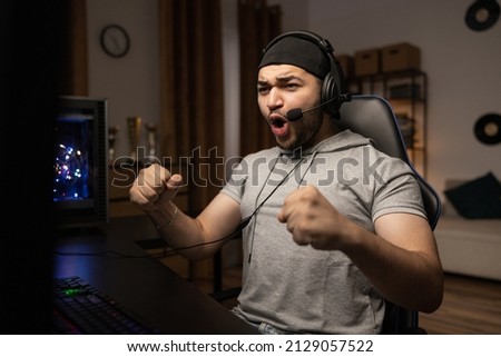 A professional player with a headset playing and winning a video game on his computer. Online championship in a virtual world. Clenched fists with joy at the victory shout