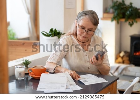 Elderly woman pays bills by phone Royalty-Free Stock Photo #2129065475