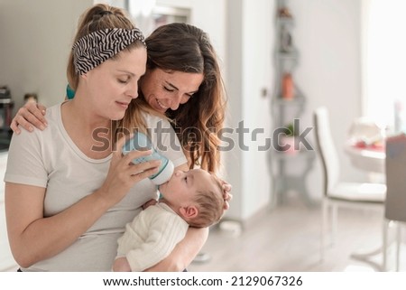 A lesbian couple giving a bottle of milk to their baby, gay marriage, gay parents and adoption concept