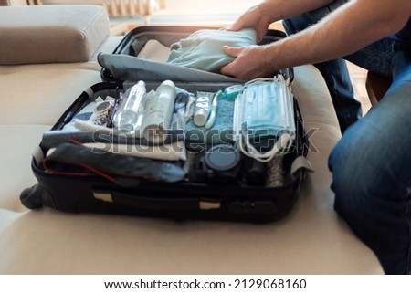 Cropped shot of a young men arranging clothes in suitcase for travel. Rear view of a man packing suitcase for business travel including face masks and airplane travel-sized antibacterial hand gels. Royalty-Free Stock Photo #2129068160