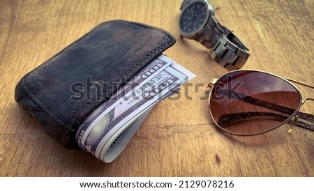 Straight view of an old wallet with bank notes. Glasses, watch and brown wood desk background.