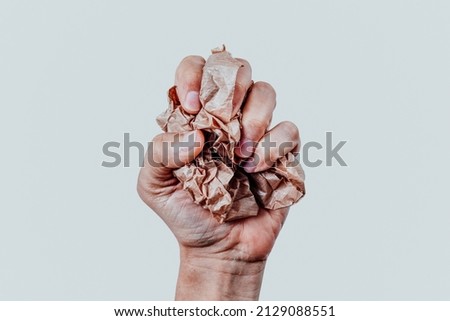 closeup of a man squeezing a ball of brown paper in his hand in front of an off-white background Royalty-Free Stock Photo #2129088551