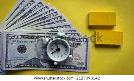 Top view of alarm clock with bank notes on yellow background. Copy space concept