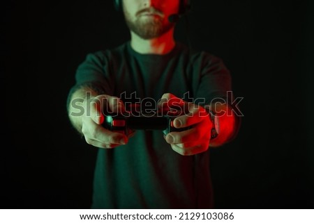 Faceless photo of a bearded man wearing headset and playing with joystick. Dark background and red light.
