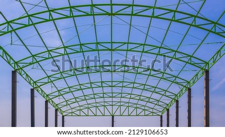 Low angle view of green metal roof beam structure of industrial building against blue sky in construction site