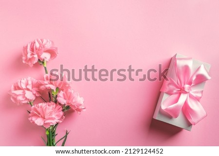 Mother's Day, Women's or Valentine's Day design concept, beautiful pink carnation flowers and gift box on pastel pink background, top view, flat lay, copy space.