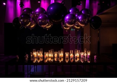 Glass jar's with burning candles light the room, making romantic and warm atmosphere at gala dinner, wedding, restaurant or event. Luxury decoration with balloons above candles. Royalty-Free Stock Photo #2129157209