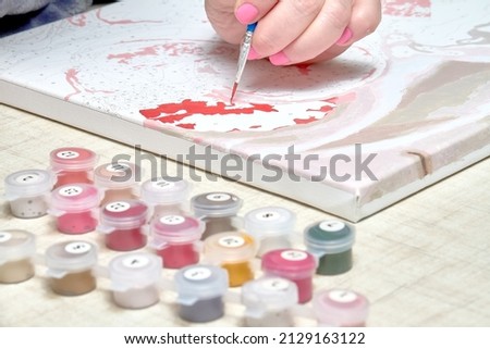 Girl with a brush and red paint draws a picture by numbers, resting.