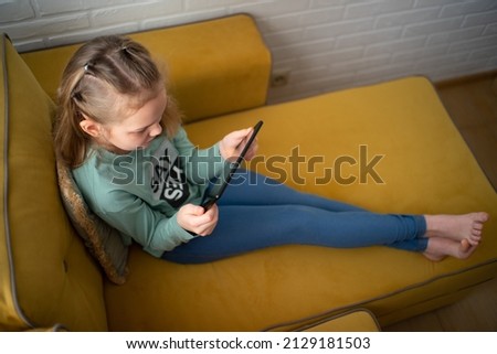 slightly overhead view of a teenage girl in casual clothes using a tablet, addicted to playing or watching a video while sitting on the sofa in the room.