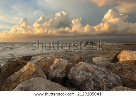 Seascape in Tuscany during the golden hour after a storm. A Trabucco (fishing mashine) in the background. Clouds in the sky. Rocks on the foreground Royalty-Free Stock Photo #2129205041