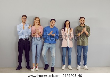 Friendly and happy young successful people stand in line and applaud their leader. Variety of casual young people standing in row near wall are smiling and proudly applauding without looking at camera Royalty-Free Stock Photo #2129205140