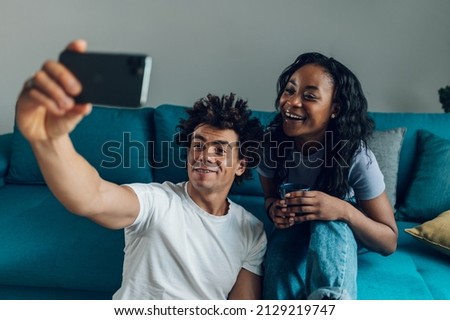 Portrait of an african american couple taking selfie with a smartphone while spending their free time together at home on the couch. Relaxing on the sofa.