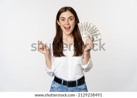 Enthusiastic woman showing money, cash and smiling, got loan, micro credit, standing delighted against white background Royalty-Free Stock Photo #2129238491