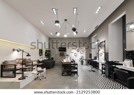 Modern interior of the beauty salon which consist of nail salon and barbershop with black lamps and concrete wall. Mirrors, chairs, backwashes and other equipment are in the salon.