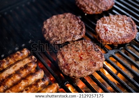 Smoky hamburger meat grilling for burgers. Fry on an open fire on the grill - bbq.Burgers and sausages Cooking Over Flames On The Grill. Royalty-Free Stock Photo #2129257175