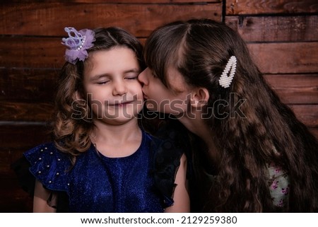 Portrait of two children girls. The older sister kisses the younger sister.