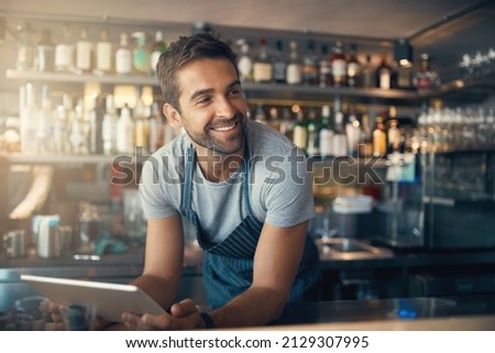 Business is right where he wants it. Shot of a young man using a digital tablet while working behind a bar counter.