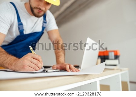 Close up of hands of repairman writing down details of an order on the clipboard while standing indoors during renovation work Royalty-Free Stock Photo #2129328176