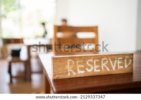A wooden sign written with the word reservation with chalk. Behind the sign there is a blurry image of a person. Hand-written wooden sign for table reservations. Re-opening the shop after the epidemic