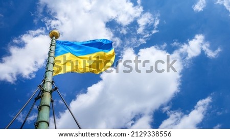 Ukrainian flag fluttering on the wind on the old flagpole against blue dramatic sky