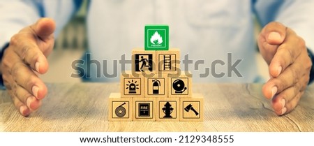 Cube wooden toy block stack in pyramid with hand protect with fire icon and door exit sing or fire escape with prevent and fire extinguisher and emergency protection symbol for safety and rescue. Royalty-Free Stock Photo #2129348555