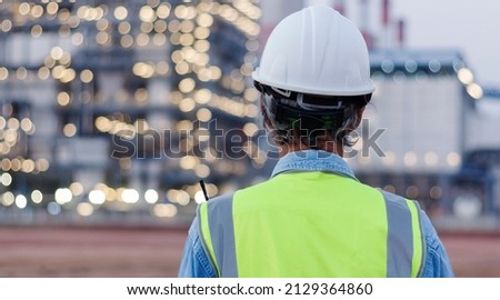 Back view, senior engineer wearing helmet and safety vest has on power plant background. Royalty-Free Stock Photo #2129364860