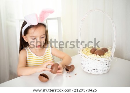 Happy Easter. Cute girl with bunny ears open breaking chocolate egg with surprise Lifestyle Light colors High quality photo
