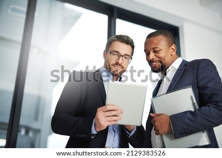 Interactive collaborations with the help of wireless technology. Shot of two businessmen using a digital tablet together at work. Royalty-Free Stock Photo #2129383526
