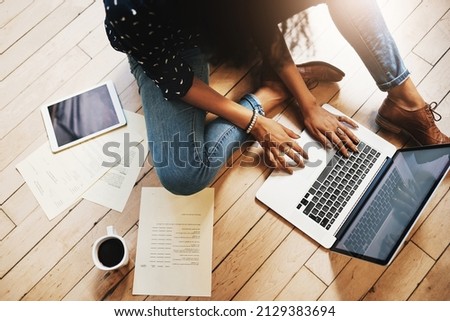 Tech savvy and industrious. Shot of an unrecognizable female designer working on her laptop while sitting on the floor in her office. Royalty-Free Stock Photo #2129383694