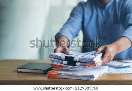 Businessman Preparing reports papers with graphs, charts on Stacks of documents files for finance in office. Piles unfinished achieves with paper clip near computer. Concept of Business Annual Report. Royalty-Free Stock Photo #2129385968
