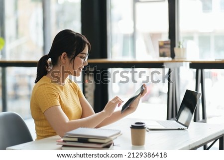 woman using laptop and tablet while relishing coffee at white desk in contemporary office