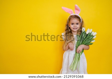 cute blonde girl with bunny ears on Easter day holding flowers white tulips in her hands on a yellow background, kid celebrate easter.