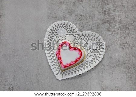 A heart shaped cookie with white royal icing and a red and pink  heart frame around it.