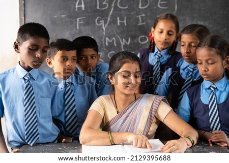 Teacher with students around explaining or teaching from book on classroom - concept of support, education, assistance and guidance Royalty-Free Stock Photo #2129395688