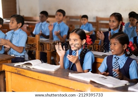 Focus on girl, young school kids in uniform applauding or clapping at classroom - concept of growth, entertainment, inspiration and childhood lifestyle. Royalty-Free Stock Photo #2129395733