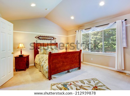 Light tones bedroom with vaulted ceiling, furnished with wood  bed.