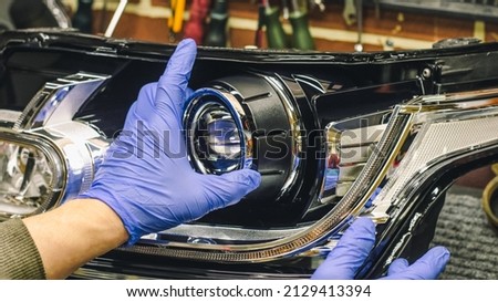 Car headlight in repair close-up. An auto mechanic wearing gloves installs the lens into the headlight housing. The concept of a car service.Installation of LED lenses in the headlight. LED lenses. Royalty-Free Stock Photo #2129413394