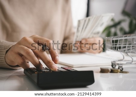 Woman counting and calculate cost money with calculator at home. Budget of disadvantaged and low income family for rising food and grocery store prices and expensive daily consumer goods concept. Royalty-Free Stock Photo #2129414399