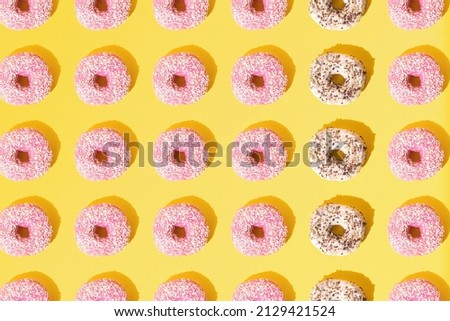 Arranged ring donuts with pink and white glaze. Small colorful crumbs on a yellow pastel background. Pattern. Flat lay.