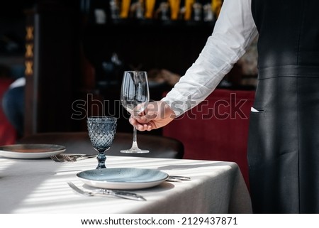 A young waiter in a stylish uniform is engaged in serving the table in a beautiful gourmet restaurant close-up. Table service in the restaurant. Royalty-Free Stock Photo #2129437871