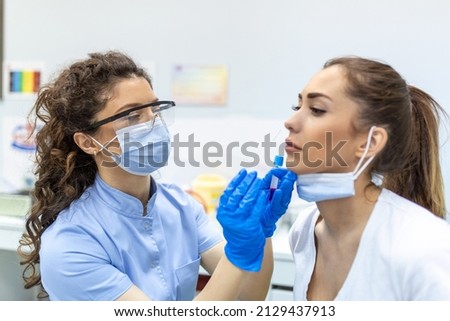 Female patient wearing mask is having sample taken from nose for a pcr test for Covid 19. Healthcare worker with protective equipment performs coronavirus swab on woman. Nose swab for Covid-19.